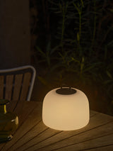 Leuchtende Nordlux Kettle To-Go 22 auf einem Holztisch im Garten am Abend
