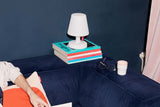 Fatboy Edison the Petit auf einem Bücherstapel neben einem dunkelblauen Sofa
